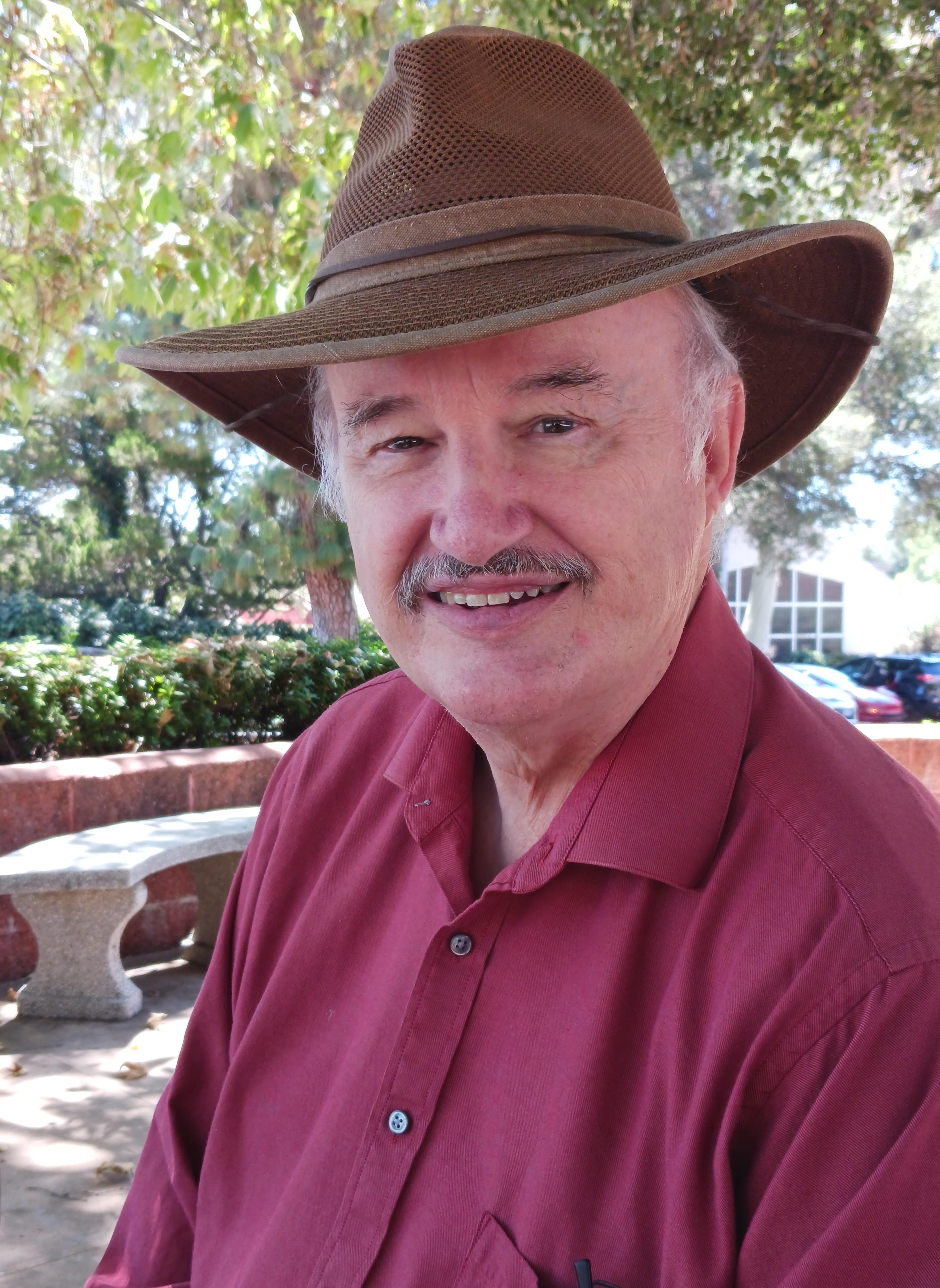 Photo of the author in a brown mesh Fedora smiling.